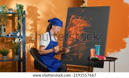 Female painter using aquarelle color to create art design on canvas, painting artistic masterpiece with paintbrush and watercolor palette. Doing artwork with skills and vision. Tripod shot.