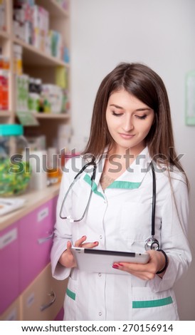 Young female doctor in pharmacy with digital tablet in hands in pharmacy interior