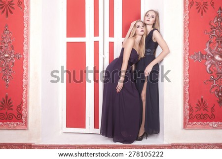 Two gorgeous girl in vintage room and cocktail dresses on a sill. Studio shooting. Beauty and fashion. Sensuality