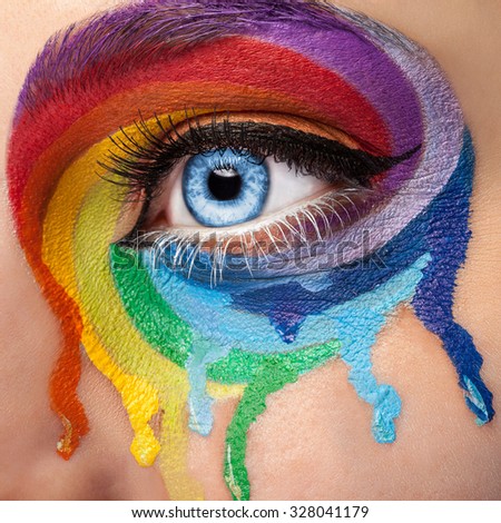 Flowing colors on an eye in fashion stage make up. Rainbow of color spectrum. Blue eye. Close up details. Macro shooting. Fashion on stage make up. Vibrant colors