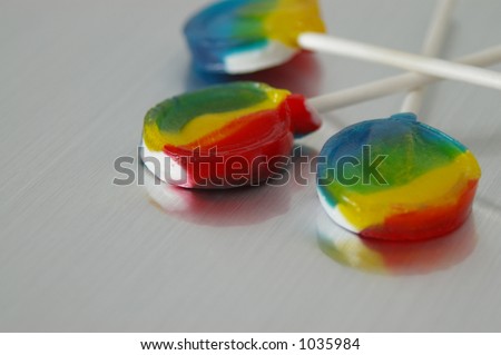 Three brightly colored lollipops over brushed metal background. With negative space for copy.