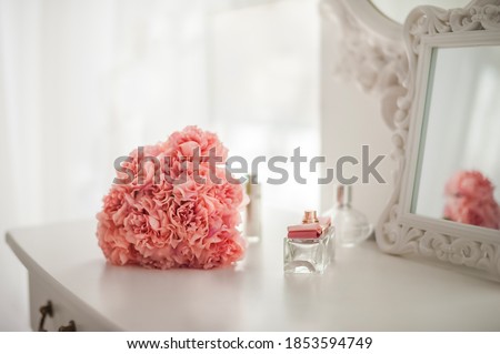 Pink flowers on the dressing table in the white bedroom. Flowers and perfumes in a bright interior. White boudoir table close up and copy space.
