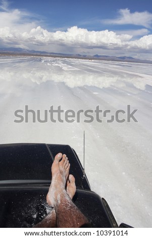 time to relax for man´s feet on a 4wd car on reflective mirrored salt lake of uyuni bolivia