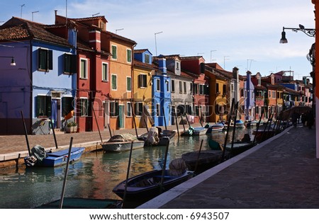 Canal on the island of Burano, near Venice, Italy. The water is flanked by small boats and multi-colored houses.