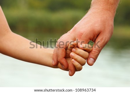 father\'s hand lead his child son against summer forest and river nature outdoor background, trust family concept