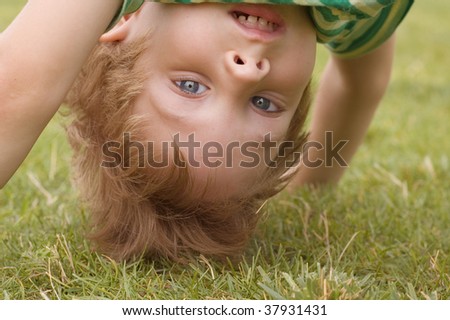 happy little boy stand on head on the summer lawn
