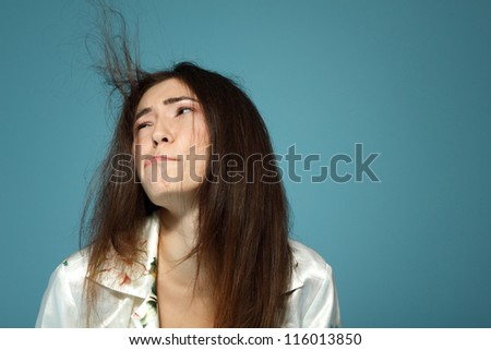 Funny teen girl has problem with her hair in the morning. Over blue background.