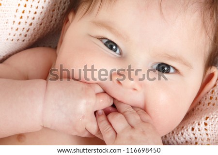 cute baby sucking fingers like a whistles lying on pink plaid, beautiful kid\'s face closeup 3 month old
