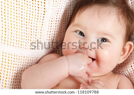 cute baby sucking fingers like a whistles lying on pink plaid, beautiful kid\'s face closeup 3 month old