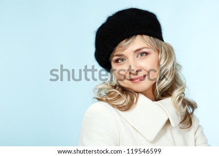mid adult happy attractive woman gives a wink, winter portrait of attractive caucasian middle aged 40 years old lady in coat and hat over blue