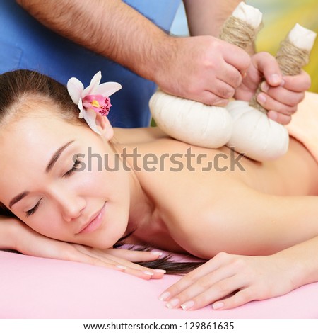 Beautiful woman enjoy having relaxing massage her back in spa salon with thai herbal compress stamps, caucasian beauty model