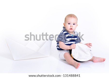 cute baby boy sitting in striped vest with ship of paper and captain cap - sailor in future, over white background