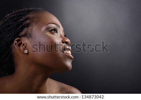 Beautiful young african woman smiling and looking up into the corner, face with hand portrait over dark background