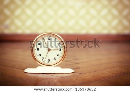 Retro clock on the weathered wooden parquet floor in vintage room with old fashioned wallpaper, toned