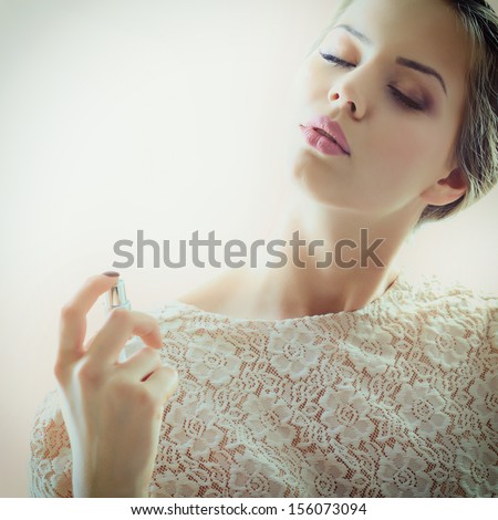 Girl with perfume, young beautiful woman holding bottle of perfume and smelling aroma, toned soft beige and noise added