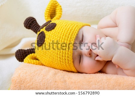 cute sleeping baby boy in funny hand made giraffe hat, beautiful kid dozing on plaid, studio shot