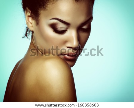 Young mulatto fresh woman with beautiful makeup looking down, isolated on blue, toned