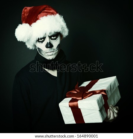 Holiday background of halloween person with terrible skull make-up in santa\'s hat with gift box over black background