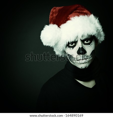 Holiday background of halloween person with terrible skull make-up in santa\'s hat box over black background