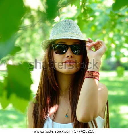 fashion girl outdoor portrait, young woman walking in summer park  in sunglasses and fedora with long brown hair