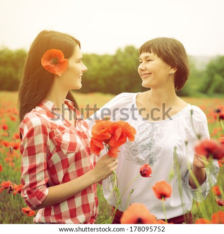 Attractive middle-aged woman has fun on a poppy field with her, summer outdoor. Image toned.