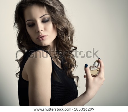 Girl with perfume, young beautiful woman holding bottle of perfume and smelling aroma, toned soft beige.