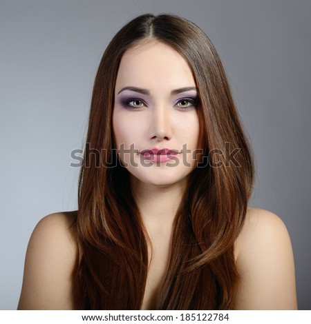 Beautiful girl. Natural beauty portrait. Young woman with beautiful healthy face and long brown hair looking at camera. Studio shot of attractive fresh girl over gray background.