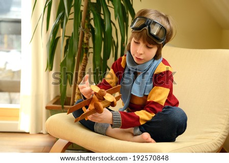 Little boy aviator dreaming and playing with wooden handmade toy plane at home