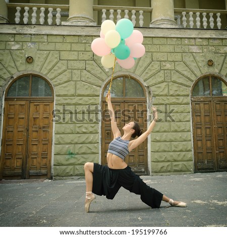 Attractive teen girl dancing outdoor in park against old building with columns holding colored balloons. Toned.
