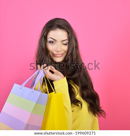 Shopping woman holding bags and gives a wink, isolated on pink studio background.