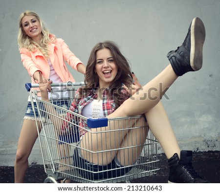 Two happy beautiful teen girls driving shopping cart outdoor, Image toned and noise added.