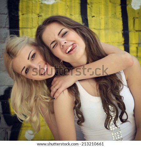 Two happy beautiful teen girls having fun outdoor against colored wall, image toned.