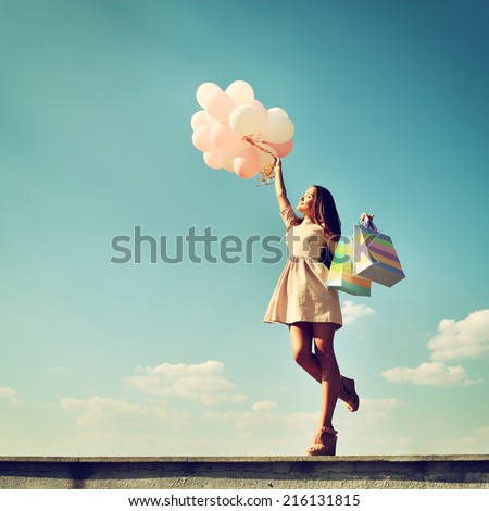 Beautiful girl holding shopping bags and colored balloons over blue sky, toned
