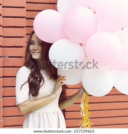 Happy young woman standing over red brick wall and holding pink and white balloons. Pleasure. Dreams. Toned.