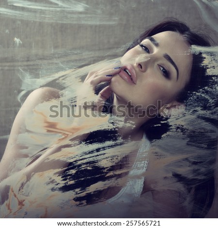 Beautiful young sensual woman on canvas behind painted window glass, image toned.