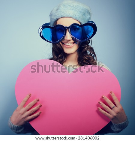 Cute attractive fashion young girl posing with funny big love glasses and pointing at pink heart