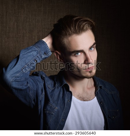 Portrait of beautiful charming young man with blue eyes and fair hair over canvas background