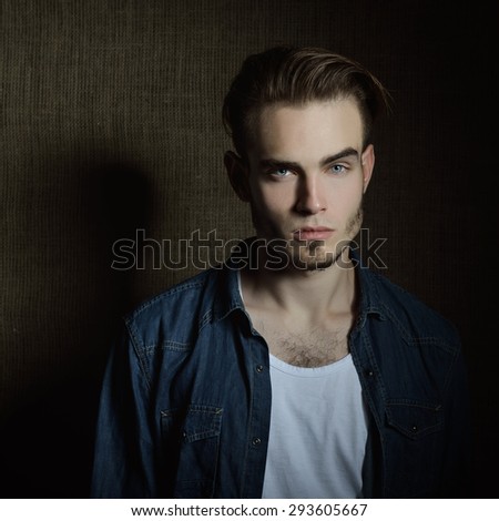Portrait of beautiful charming young man with blue eyes and fair hair over canvas background