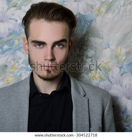 Portrait of attractive young man bites his lip and looking at camera, over floral background. Image toned and noise added.