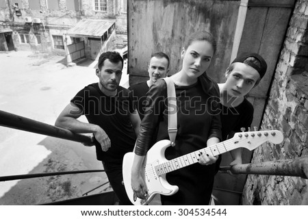 Music band outdoor portrait. Musicians and woman soloist posing outside against grunge yard, black and white.