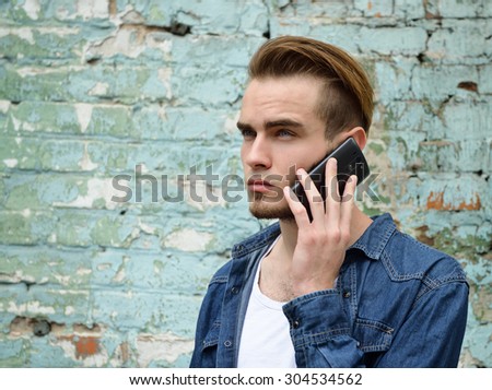 Portrait of young handsome man calling phone outdoor against grunge obsolete wall