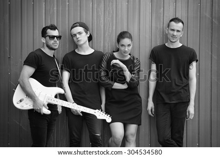 Music band outdoor portrait. Musicians and woman soloist posing outside against grunge fence, black and white.