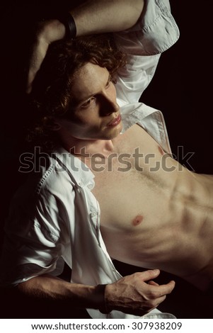Portrait of young handsome man with open white shirt and rich curly hair over black background. Image toned.