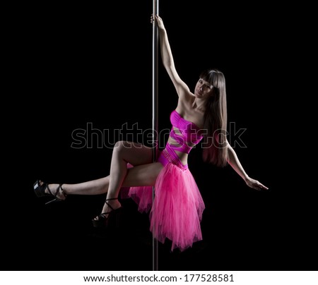 Beautiful young pole dancer smile and rotates in a bright pink dress and develops chiffon skirt. Black background. Studio shot. Low-key lighting. Dark colors