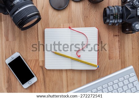 Top view of a desktop of a photographer consisting on a cameras, a keyboard, a smart phone  on a wooden desk background