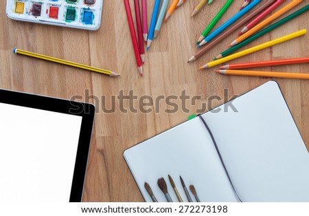 Designer workspace with tablet and watercolors on wooden desktop