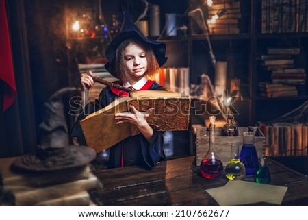 Surprised caucasian little girl in witch Cosplay reads magic book while holding magic wand, Halloween costume. Halloween party. Foto stock © 