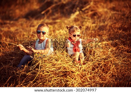 Summer landscape with hay cocks, couple children, brother and sister sitting on large pile of hay