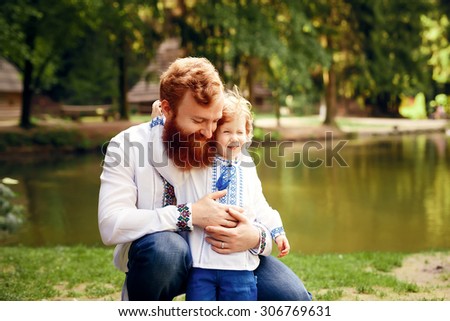 Red-heared father and red-heared son having fun in a park in a traditional white shirts with ornament