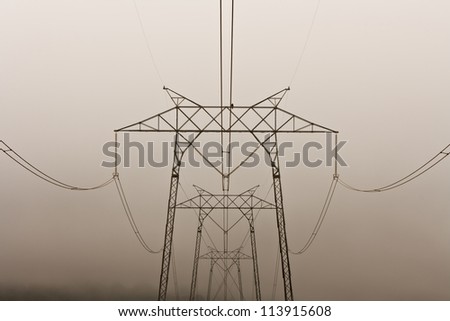 Electrical lines hang from a series of steel electricity pylons on a foggy morning.